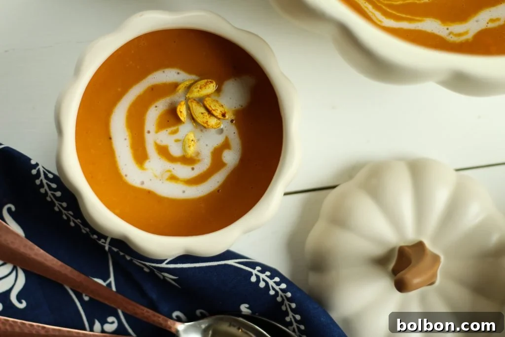 A beautifully plated bowl of Roasted Pumpkin Coconut Curry Soup, garnished with a drizzle of coconut cream, a sprinkle of fresh herbs, and curry roasted pumpkin seeds.