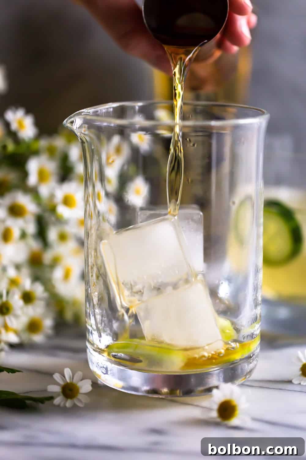 Irish whiskey being poured over ice into a cocktail mixing glass.