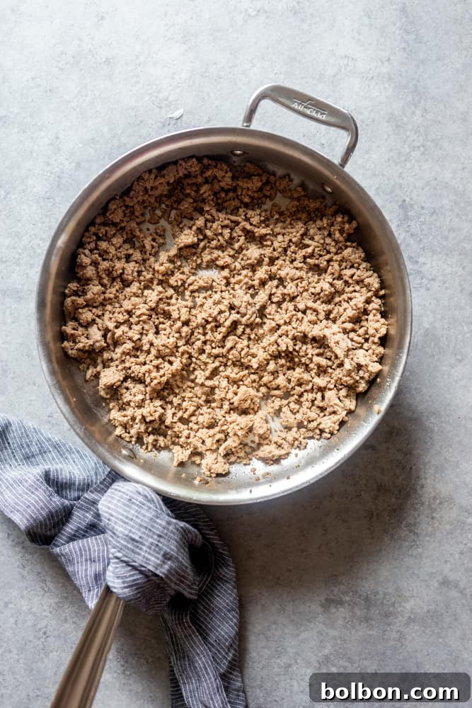 Ground turkey being expertly browned in a large, non-stick frying pan, showing the meat crumbling and cooking evenly