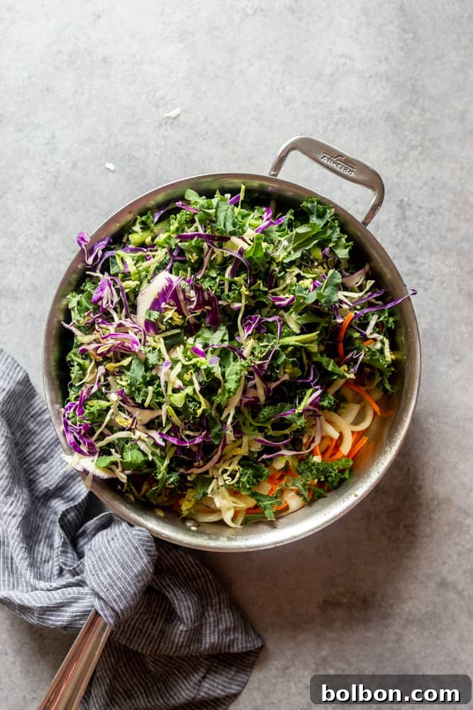 A vibrant mix of shredded carrots, green and red cabbage (coleslaw mix) being stir-fried with sautéed onions in a large pan