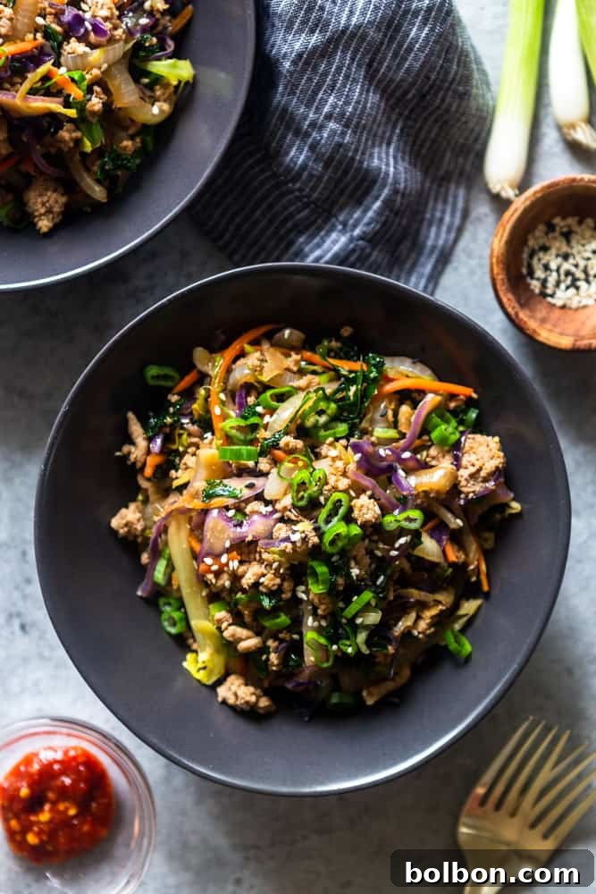 Beautifully plated Egg Roll in a Bowl recipe in elegant black ceramic bowls, garnished with toasted sesame seeds, fresh green onions, and accompanied by a small dish of chili garlic sauce for customizable spice, showcasing a complete and appealing meal