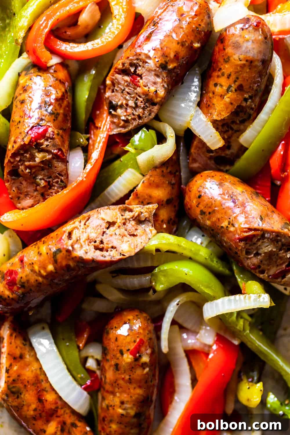 Roasted Sausage, Peppers and Onions Close-up of golden brown sausages nestled among tender, roasted bell peppers and onions on a sheet pan.