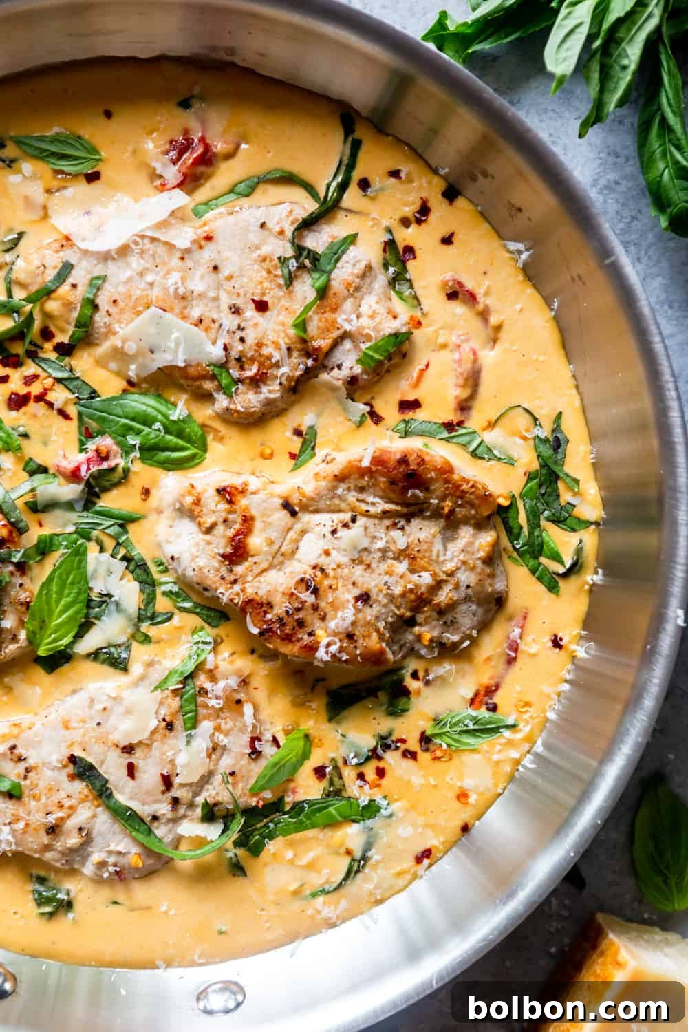 Juicy boneless pork chops swimming in a creamy parmesan basil sauce in a skillet, garnished with fresh basil.