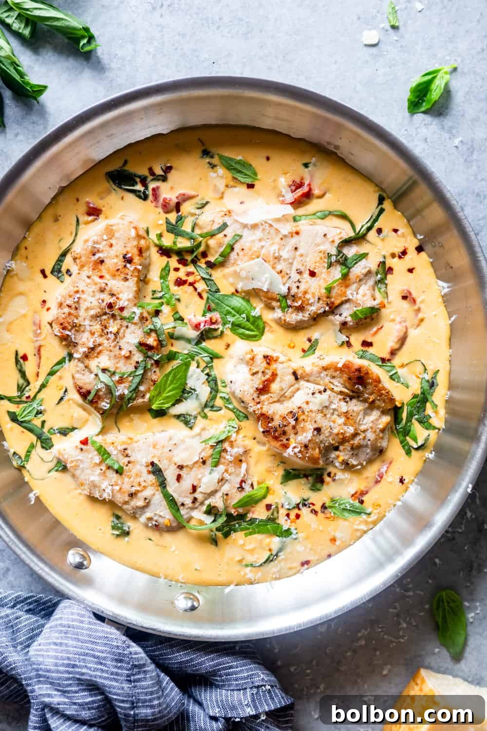 Skillet filled with creamy parmesan basil sauce, with seared pork chops nestled within, ready to be served.