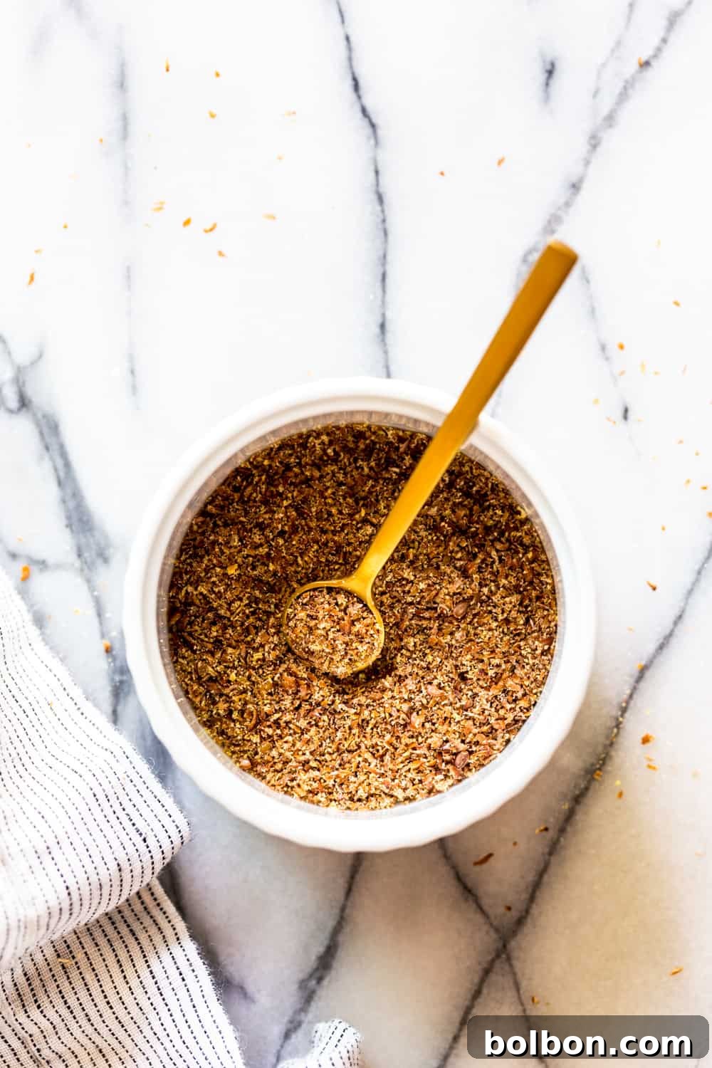 Ground flaxseed in a white bowl with a gold spoon, ready to be mixed for a flax egg.