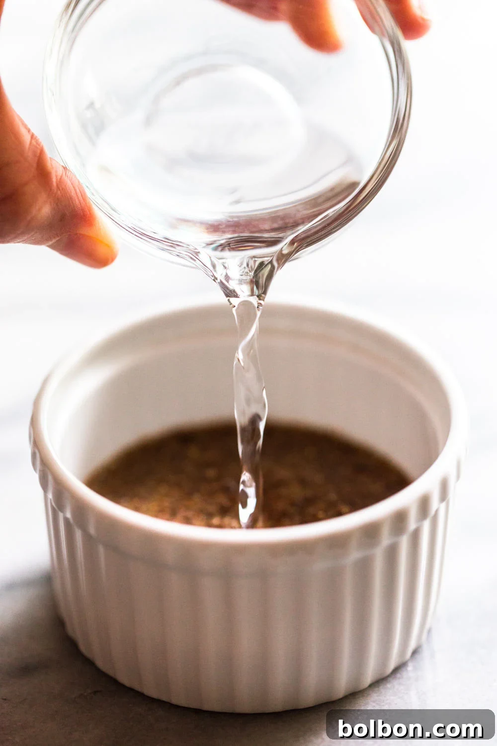 Water being poured into a white bowl containing ground flaxseed, illustrating the mixing process.