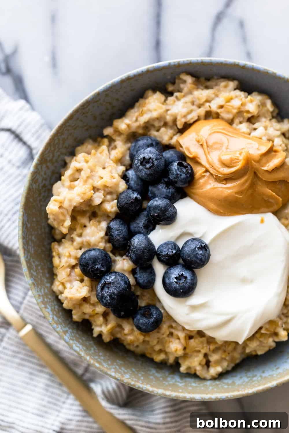 Quick and Creamy Instant Pot Steel Cut Oats 6 Oatmeal topped with yogurt, peanut butter and blueberries in a light blue bowl with a gold spoon