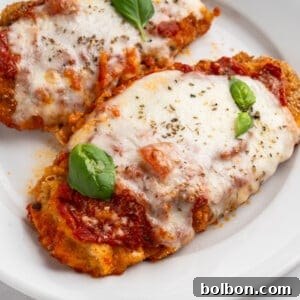 Two breaded chicken parmigiana covered in melted mozzarella cheese and tomato sauce, garnished with fresh basil leaves, served on a white plate.