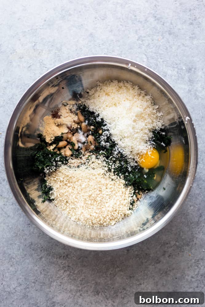 The mixture for white bean and kale burgers in a gleaming silver bowl, displaying the texture and combination of mashed beans, chopped kale, and other ingredients before shaping.