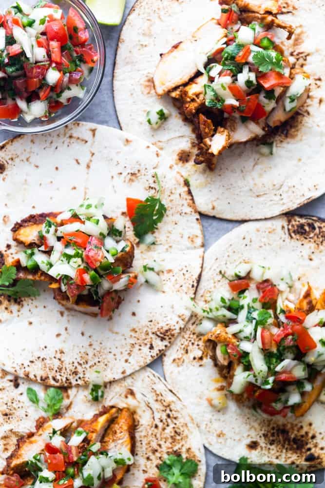 A stack of corn tortillas generously filled with tender chili lime chicken, topped with fresh pico de gallo, showcasing a vibrant and delicious chicken taco.
