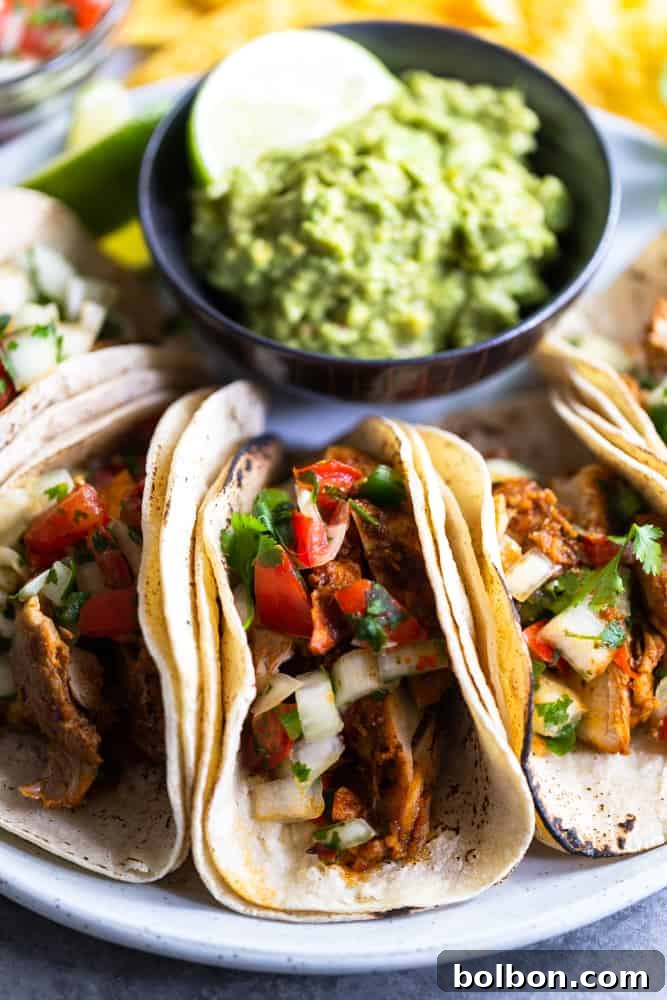Close-up of a delightful chili lime chicken taco on a pristine white plate, accompanied by a small serving of vibrant green guacamole, highlighting the fresh and appealing toppings.