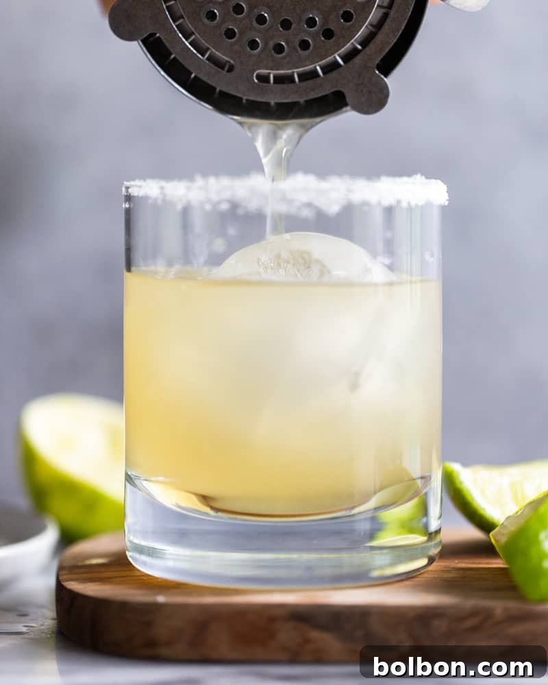Effortless Homemade Margarita Recipe 3 A bartender pouring a freshly shaken margarita from a cocktail shaker into a salt-rimmed glass filled with ice, ready for enjoyment.