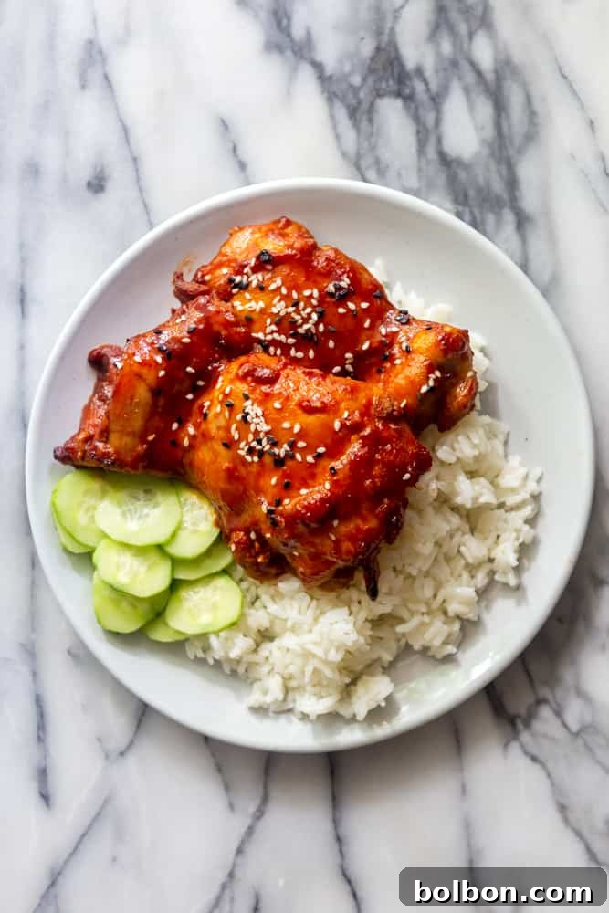 Korean chicken thighs on a white plate with rice and cucumbers