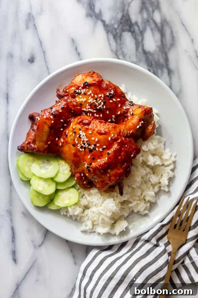 Sticky Korean Thighs on a white plate with white rice and sliced cucumbers.