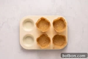 A muffin tray with six cups, four filled with brown cupcake batter in parchment liners and two empty, sits on a light marble surface.