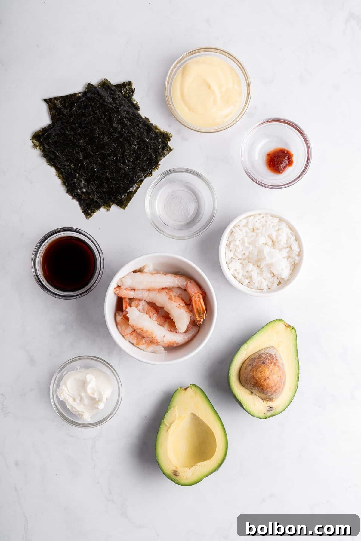 Ingredients for sushi: nori sheets, mayonnaise, soy sauce, shrimp, cooked rice, avocado halves, cream cheese, and a small dish with red chili paste, all arranged on a light marble surface.