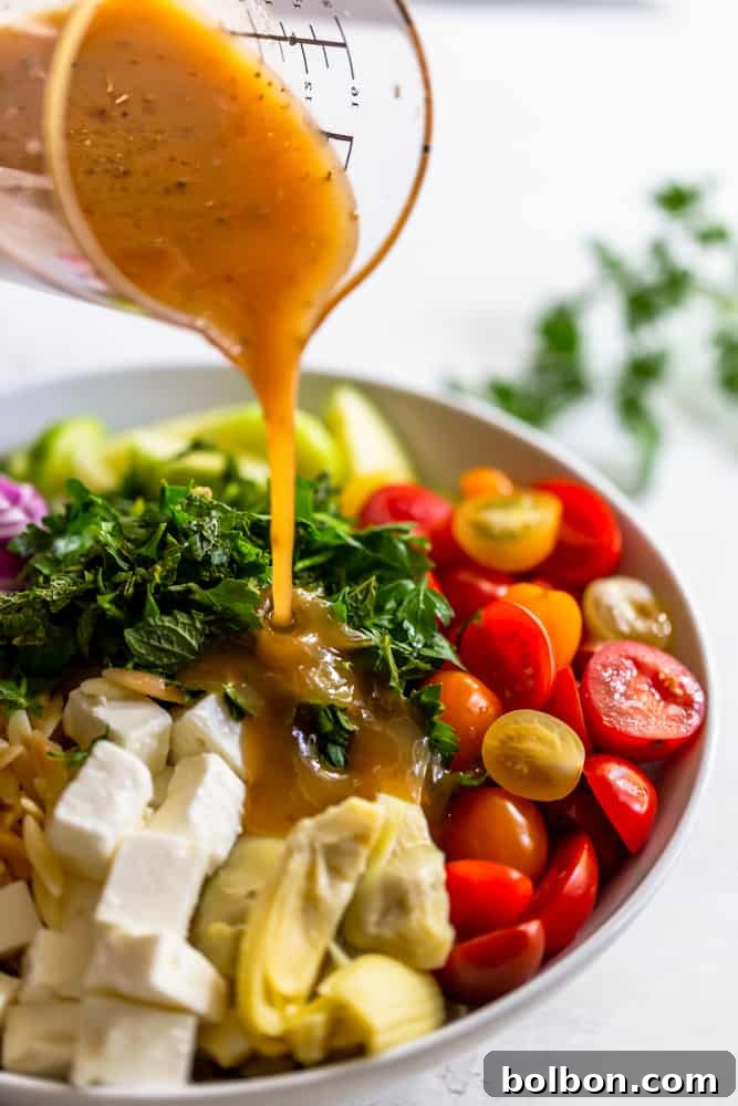 Vibrant Mediterranean Orzo Salad 5 Close-up shot of the vibrant lemon dressing being poured generously over the prepared Mediterranean Orzo Salad, showcasing its rich coating of fresh ingredients