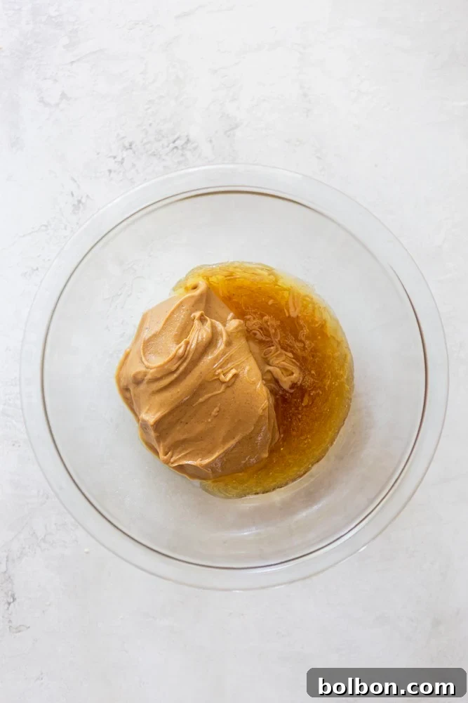 Honey-Sweetened Peanut Butter Power Bites 3 Peanut Butter and honey being mixed in a glass bowl, illustrating the first step of the recipe