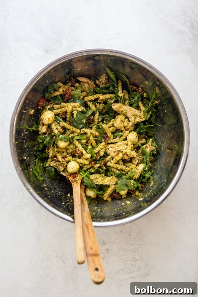 Generous portion of Chicken Pesto Pasta Salad freshly mixed in a large stainless steel bowl