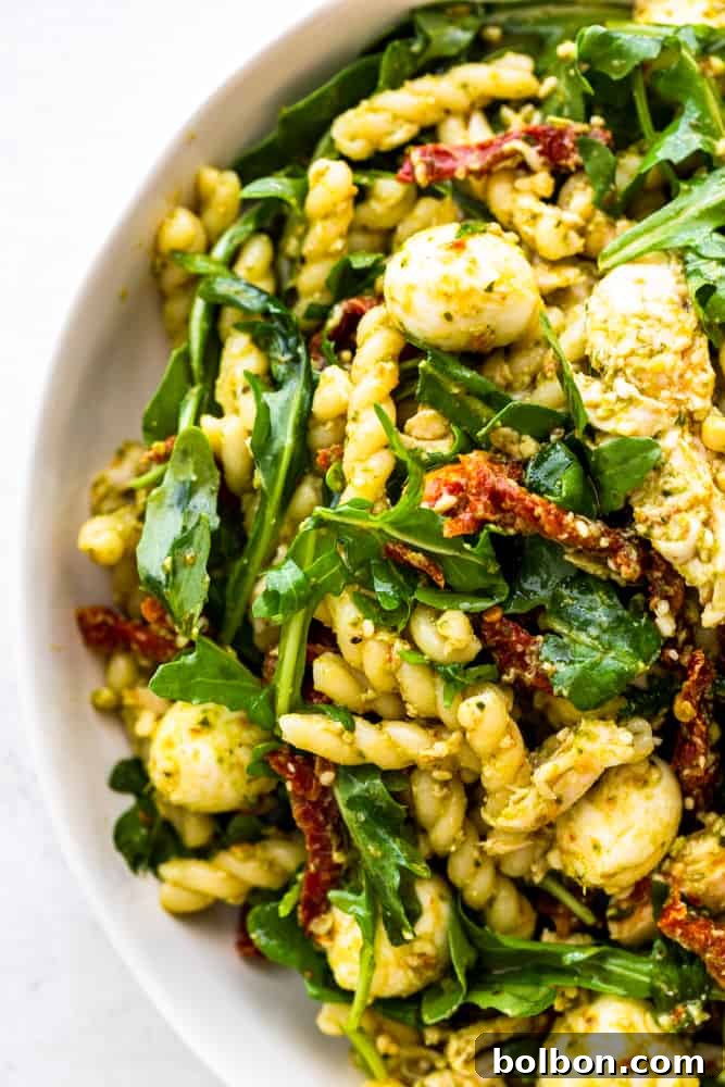 Close-up of a serving of Chicken Pesto Pasta Salad in a white bowl, showcasing the textures and colors of the ingredients