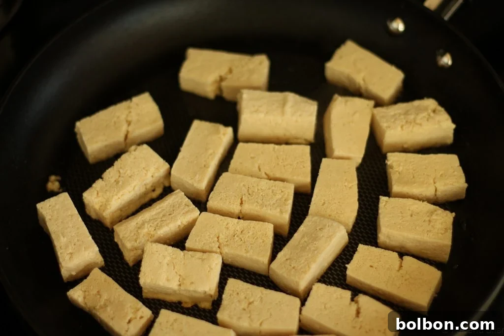 Perfect Tofu Secrets 11 Tofu pieces sizzling in a hot skillet with oil, beginning to brown on one side.