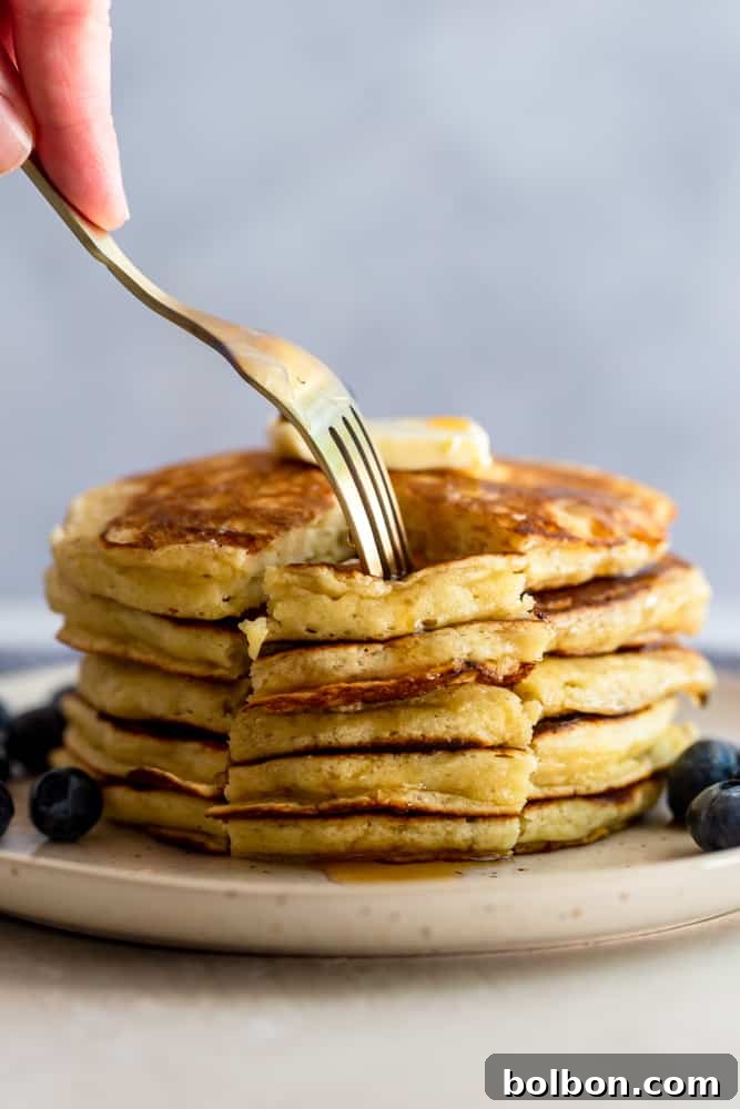 Perfectly Fluffy Buttermilk Pancakes 2 A fork pressing into a wedge of fluffy buttermilk pancakes, showcasing their soft texture and golden-brown edges.