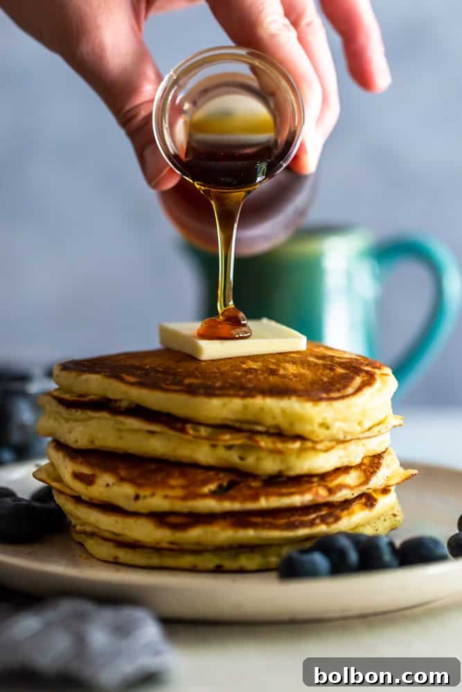 Perfectly Fluffy Buttermilk Pancakes 3 Rich maple syrup gracefully pouring over a generous stack of golden-brown buttermilk pancakes, creating a tempting breakfast scene.