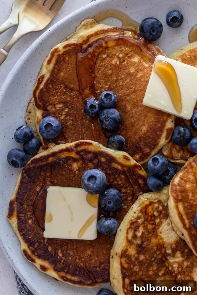 Perfectly Fluffy Buttermilk Pancakes 4 A delightful plate of fluffy buttermilk pancakes, artfully arranged with a generous pat of butter, fresh blueberries, and a drizzle of golden maple syrup.