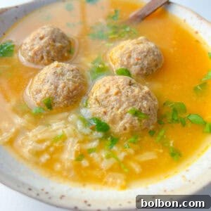 A bowl of Hidden Veggie Meatball Soup with four meatballs, rice, chopped fresh herbs, and a spoon in a light broth.