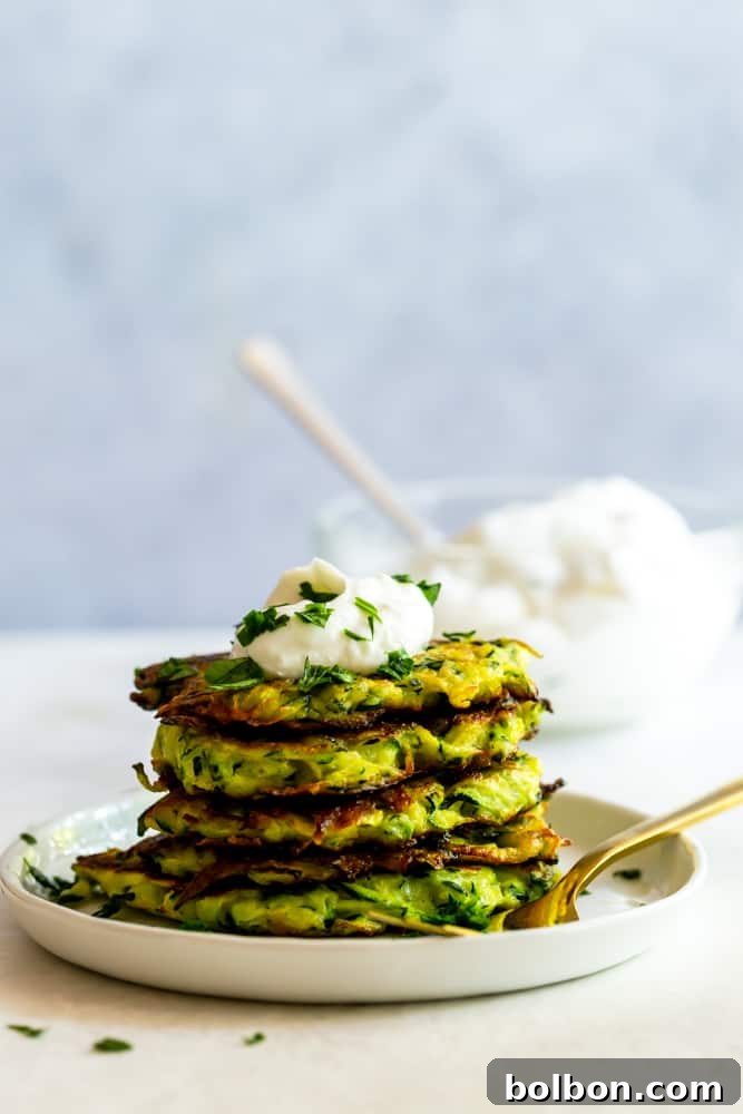 Stack of zucchini fritters on a white place with garlic yogurt sauce.