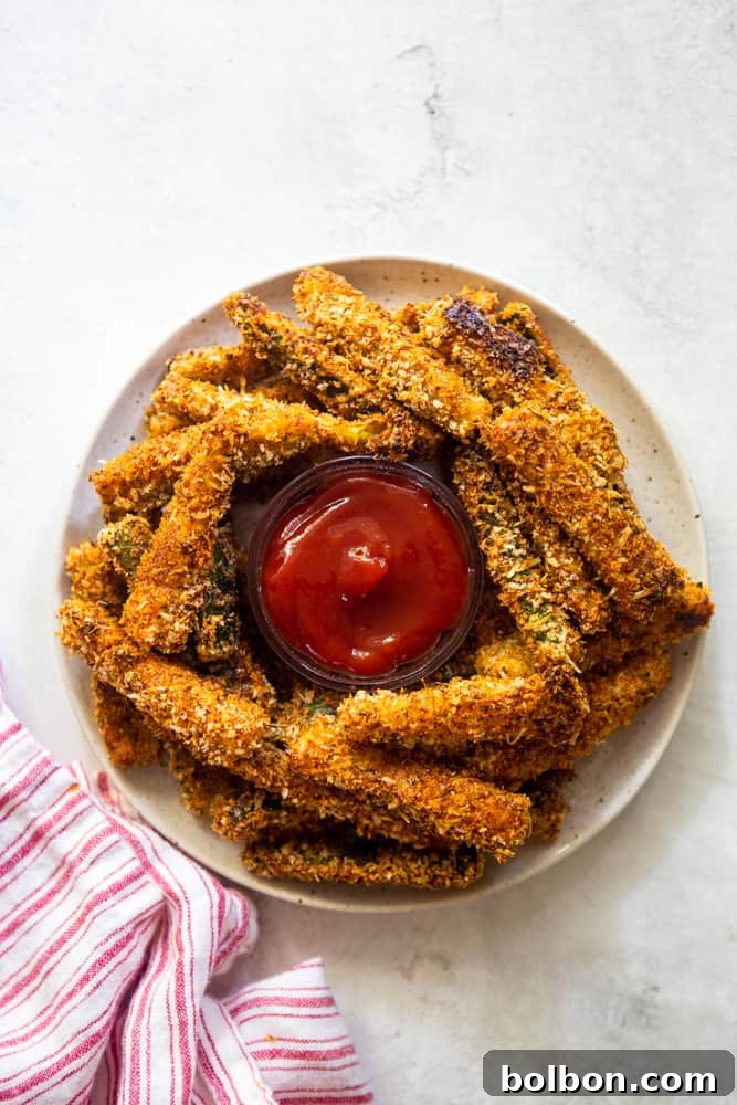 Golden Baked Zucchini Sticks 6 A close-up of a plate piled high with golden crispy baked zucchini fries, ready to be enjoyed.