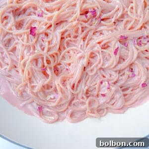 Close-up of Pink Pasta coated in a creamy, pastel pink sauce, garnished with small pink flower petals, served in a white bowl.