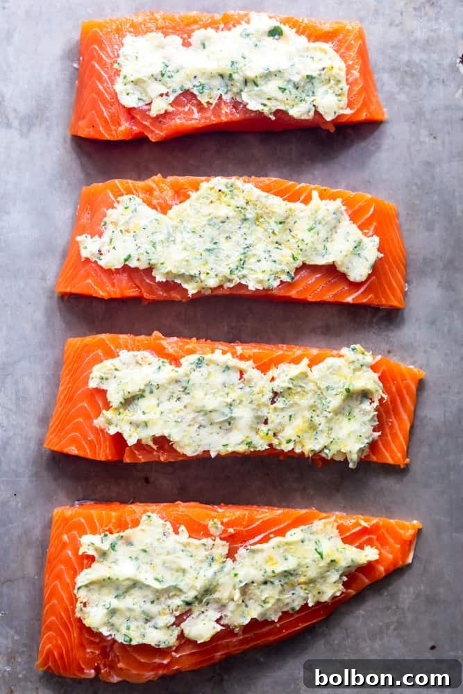 Raw salmon fillet on a baking sheet, generously coated with a vibrant garlic butter mixture, ready for the oven.