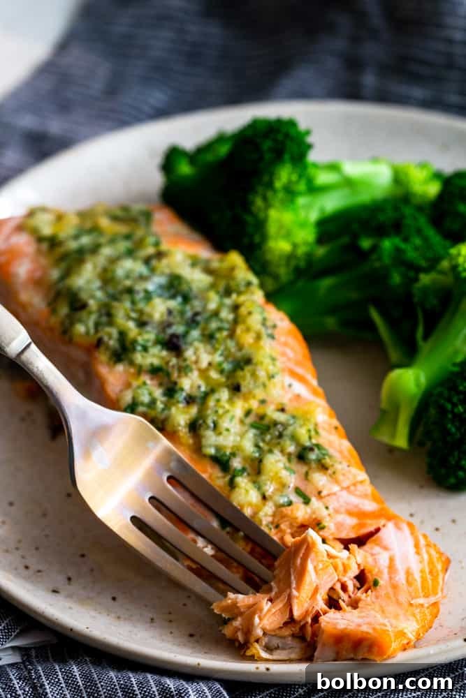 A fork gently digging into a piece of baked salmon, revealing its tender, flaky texture.