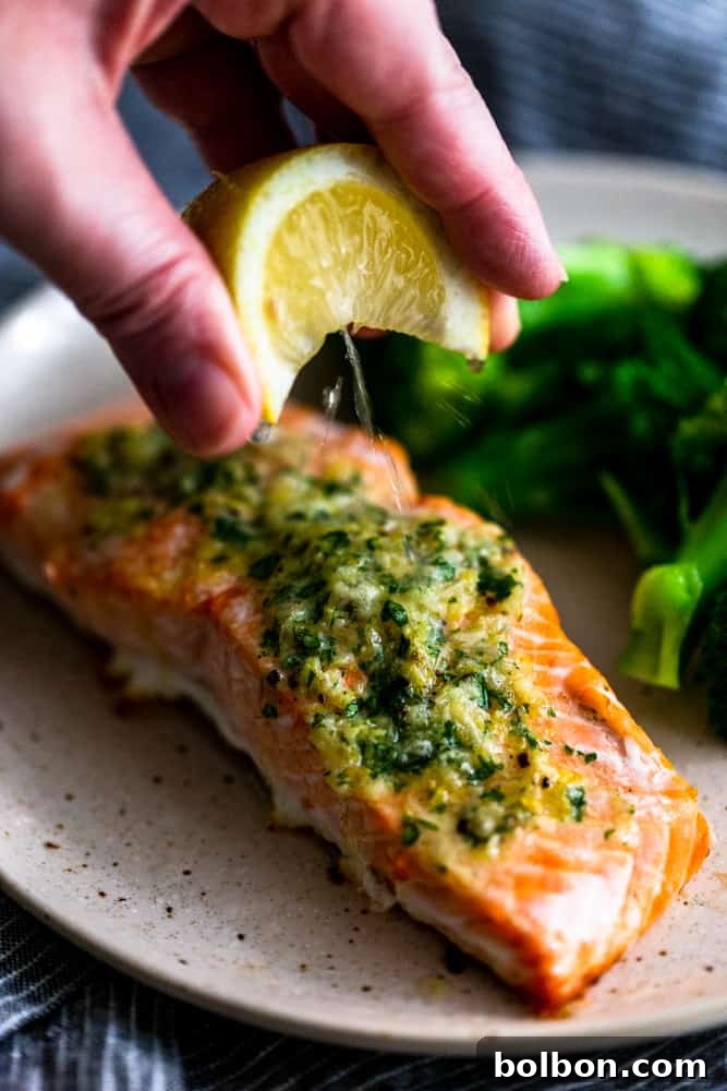 A fresh lemon wedge being squeezed over a piece of baked salmon, adding a final touch of brightness.