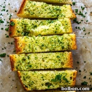 A whole loaf of homemade garlic bread, cut into slices, on a wooden cutting board