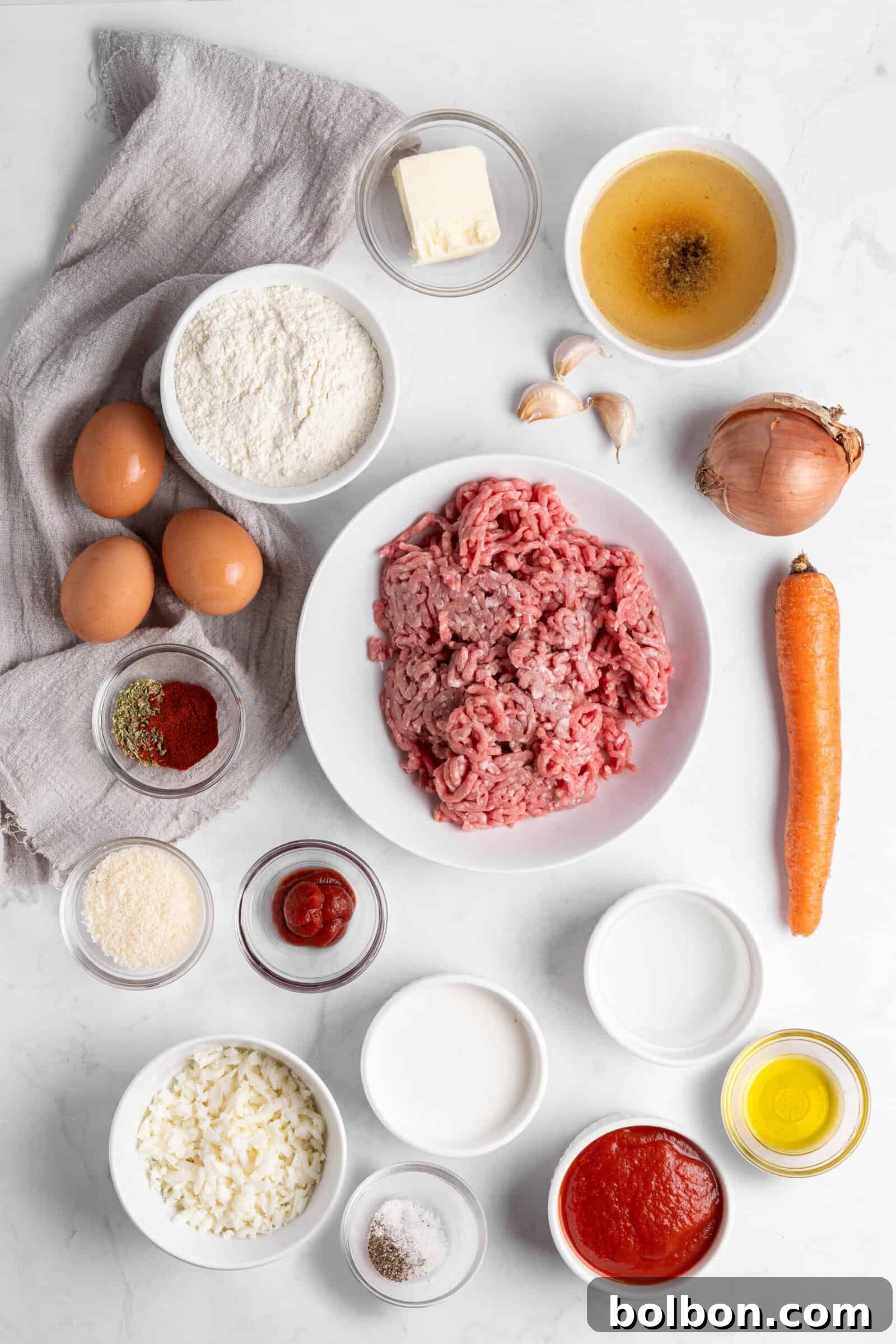 Crepe Lasagna Bake 3 Top-down view of various ingredients on a marble surface, including ground meat, eggs, flour, butter, stock, garlic, onion, carrot, spices, tomato sauce, and oil, all arranged in bowls and on a linen cloth.