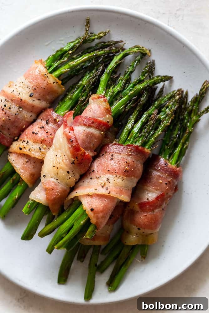 Crispy bacon-wrapped asparagus bundles on a white serving plate, garnished with fresh herbs, showcasing a perfect holiday appetizer or side dish.