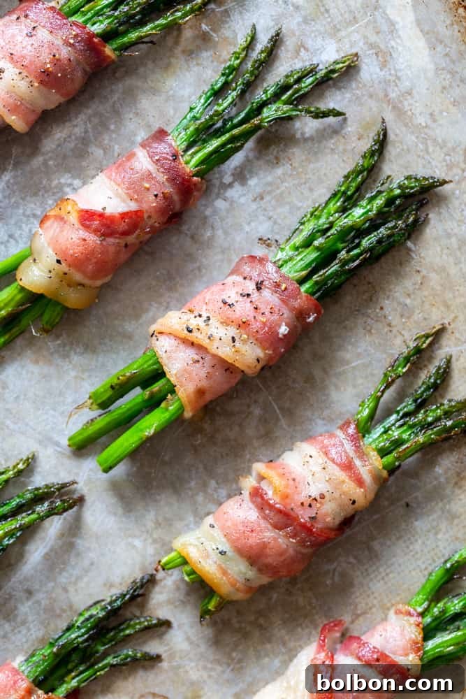 Several golden-brown bacon-wrapped asparagus bundles neatly arranged on a wire rack over a baking sheet, fresh out of the oven.