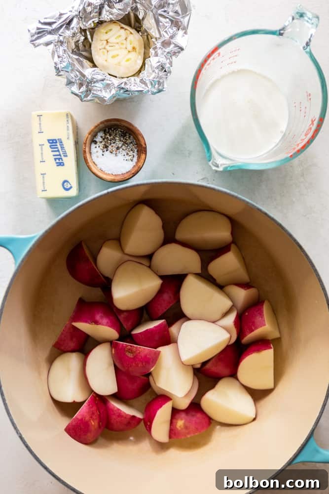Ingredients for garlic mashed potatoes: red potatoes cut into quarters in a large dutch oven, a stick of butter, salt and pepper in a small wooden bowl, half and half in a measuring cup, a head of garlic wrapped in foil. 