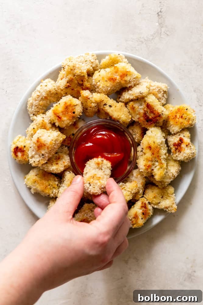Hand dipping a baked chicken nugget into ketchup