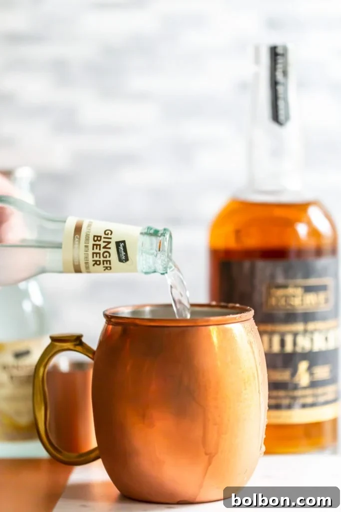 Close-up of a Gingerbread Irish Mule being stirred in a copper mug with candied ginger garnish.