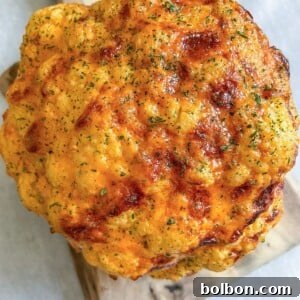 A Whole Roasted Cauliflower head with a golden-brown crust, sprinkled with herbs, rests elegantly on a wooden cutting board.