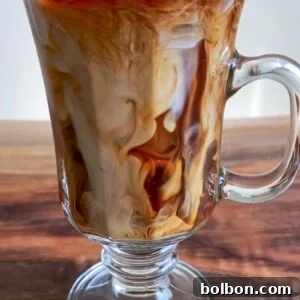 Chilled Vanilla Bliss 3 A glass mug filled with Iced Coffee with Vanilla, swirling with cream, sits on a wooden surface. The drink displays marbled patterns as the vanilla-scented cream mixes with the coffee over ice.