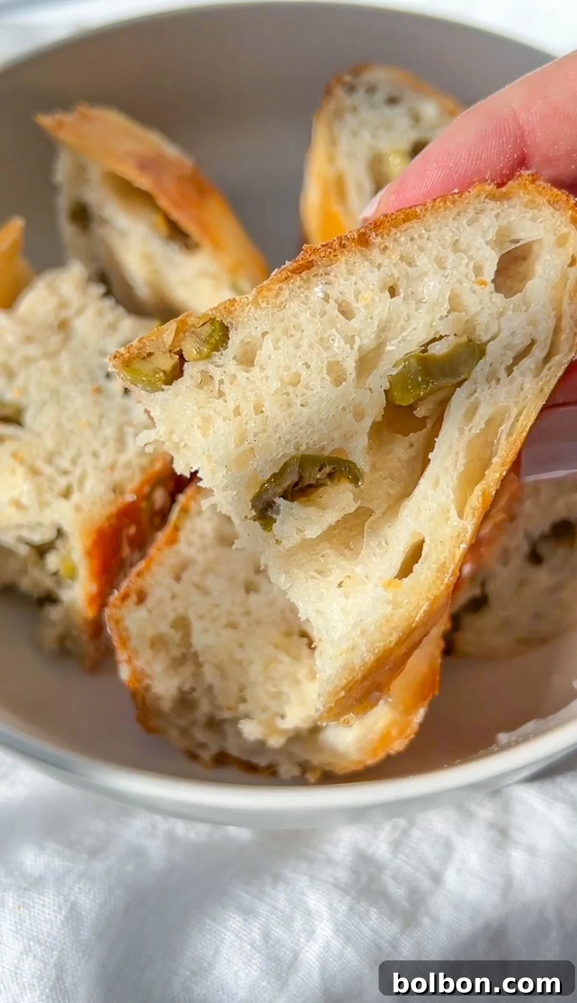 A beautifully baked No Knead Olive Bread, golden brown with visible olives, sitting on a wooden surface.