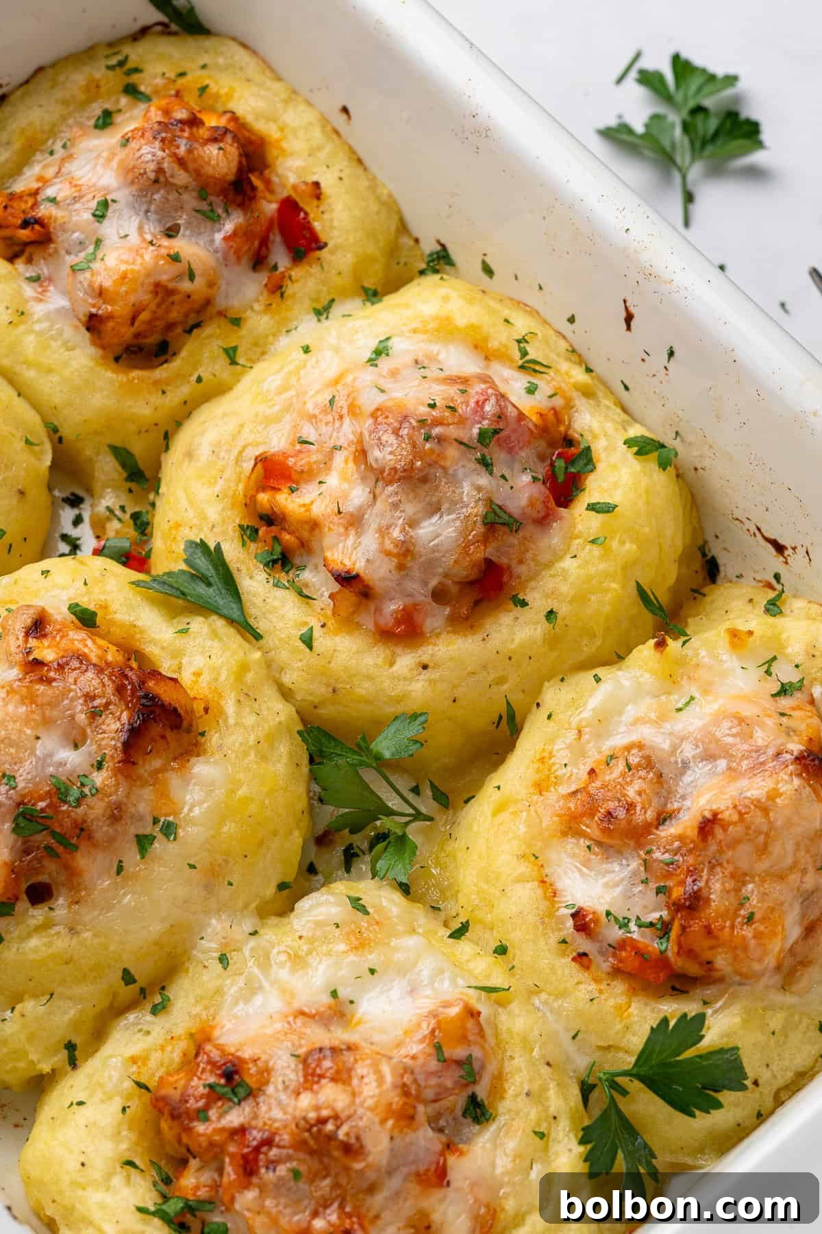 a baking dish with a close up view of the chicken mashed potato nests, golden brown, with melted cheese on top and garnished with parsley.