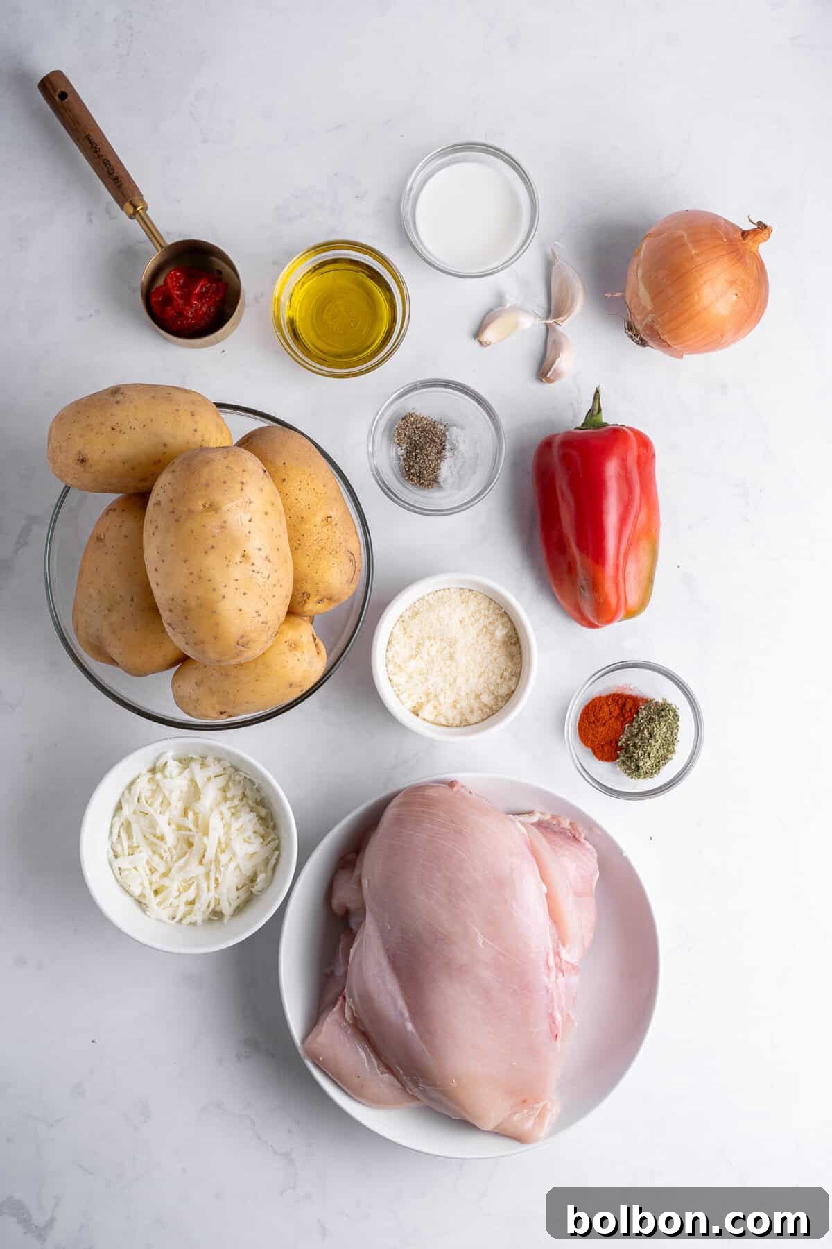 a flat lay of ingredients for the chicken mashed potato nests. Ingredients include potatoes, cheese, chicken breasts, a pepper, various spices and olive oil. 