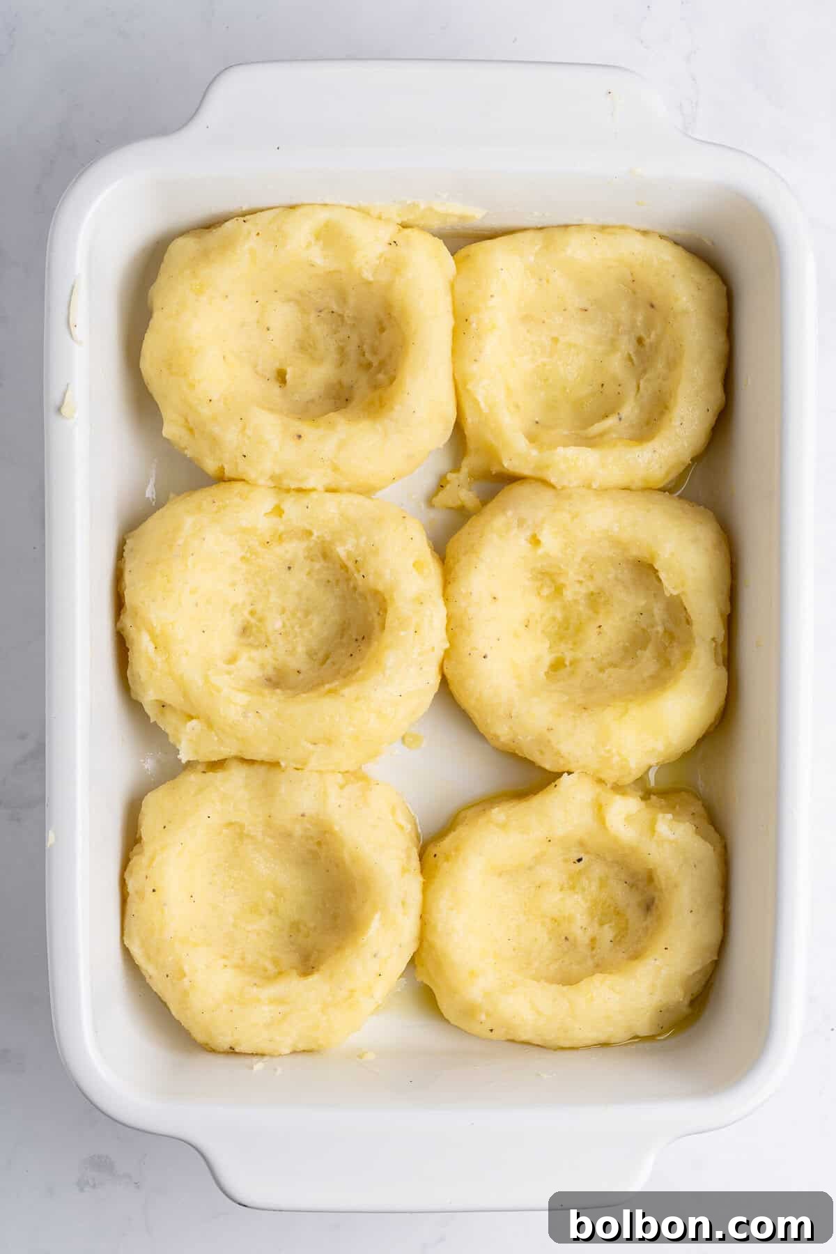 A casserole dish with 6 mashed potato nests. 