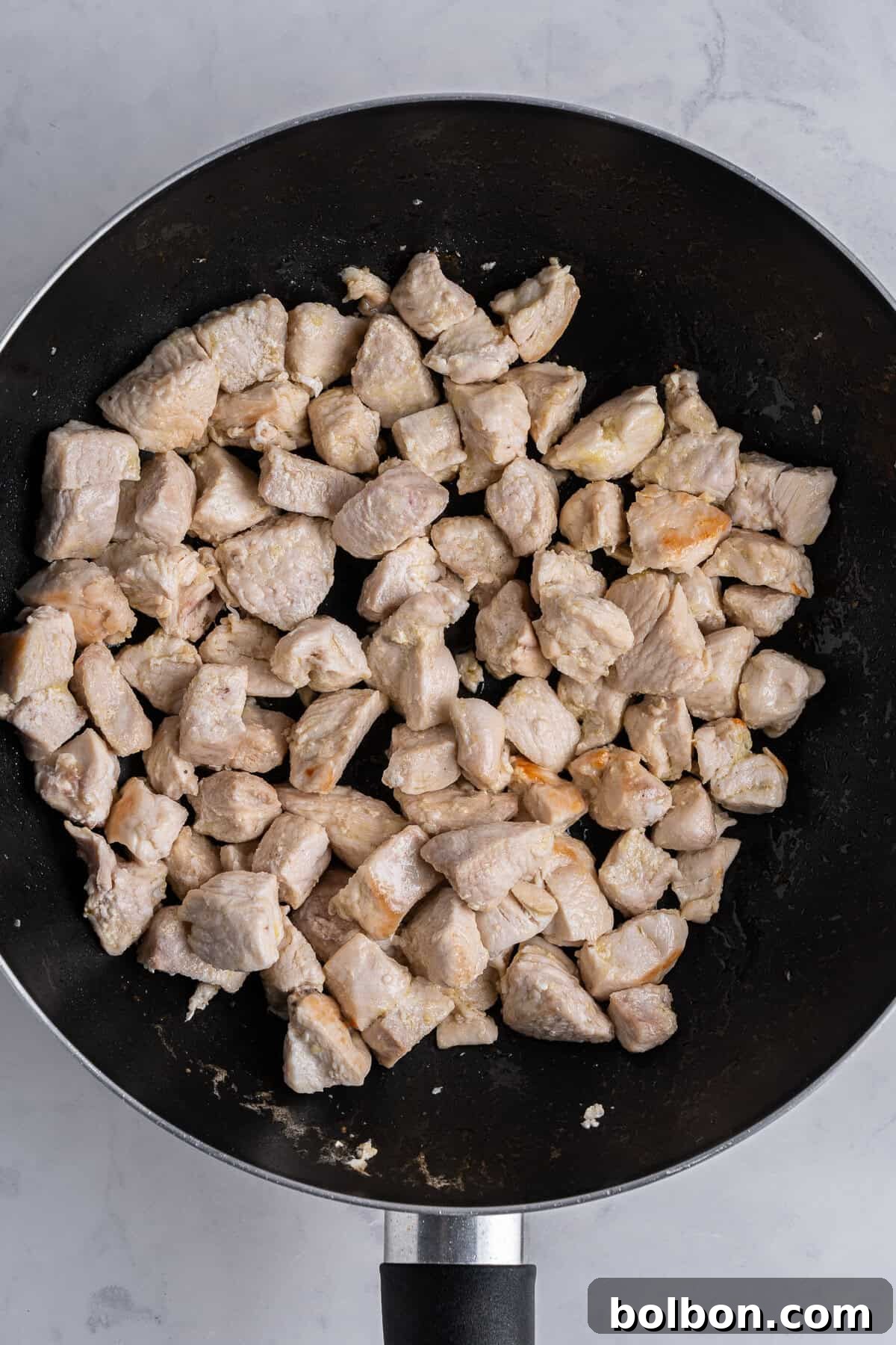 A saute pan of cubed pieces of chicken cooking.