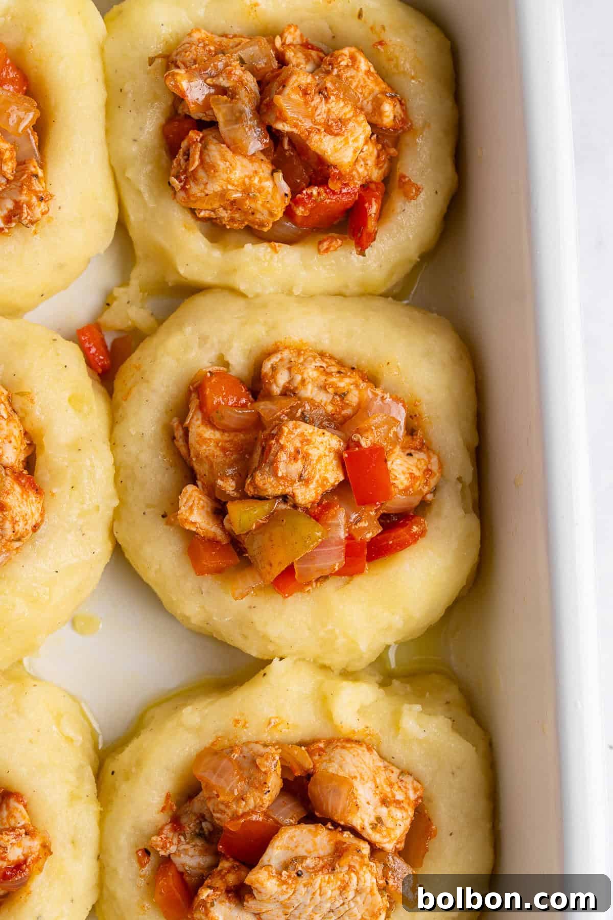 A close up of a mashed potato nest filled with a scoop of cooked chicken and vegetable mixture.  